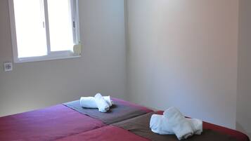 Habitación de hotel con dos camas, un televisor montado en la pared y una ventana con persianas.