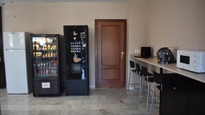 A kitchenette with a white refrigerator, a vending machine, a microwave, and a wooden door. - Hostal Alamare (Seville)