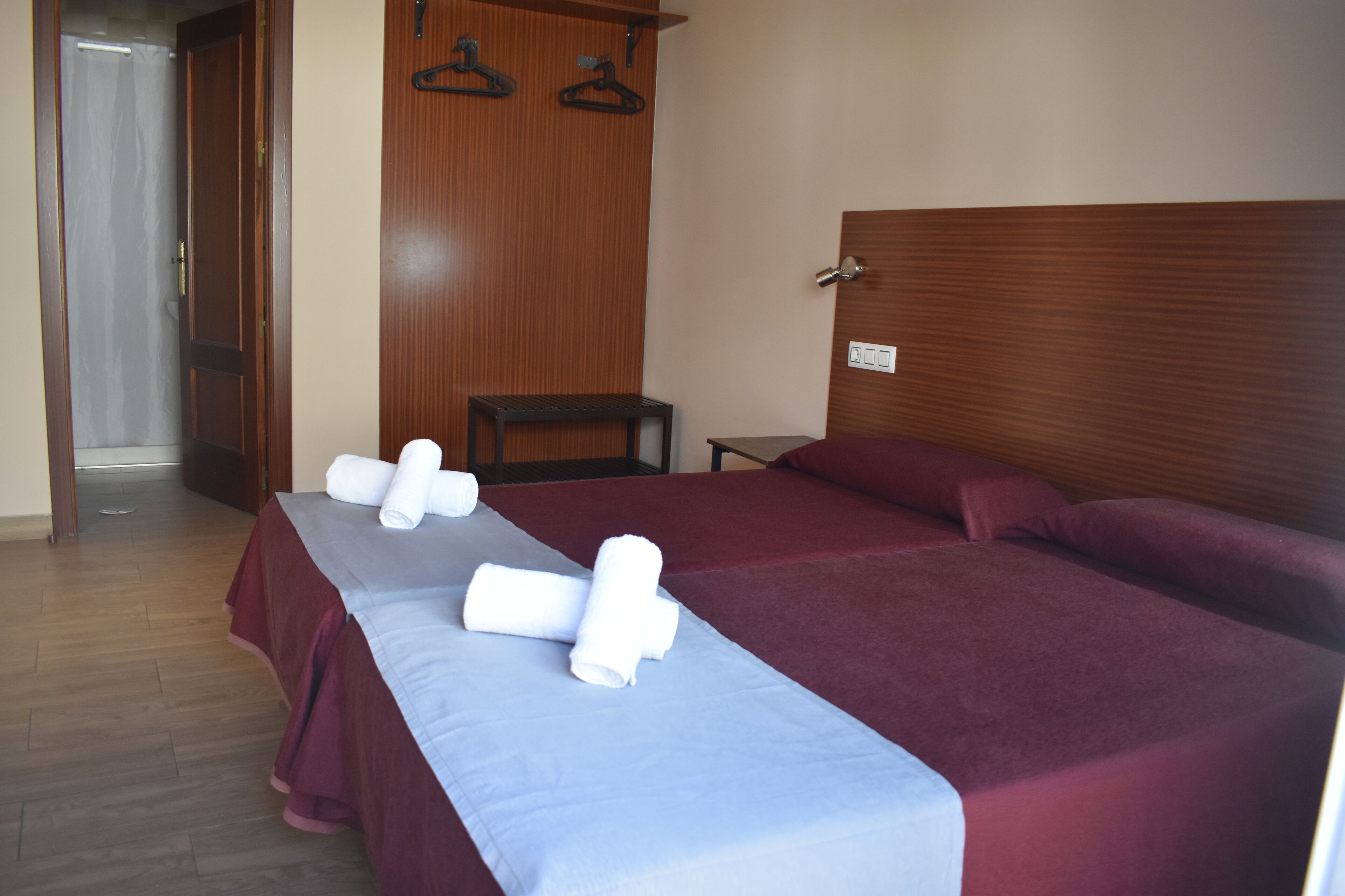 A hotel room with two beds, a wooden headboard, a small table, and a chair.