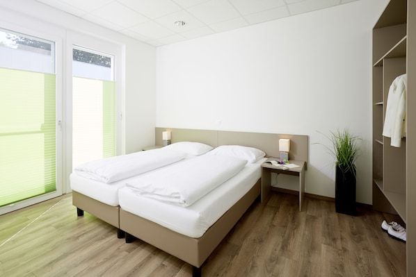 Un dormitorio con cama, mesitas de noche, una planta en maceta y un armario.