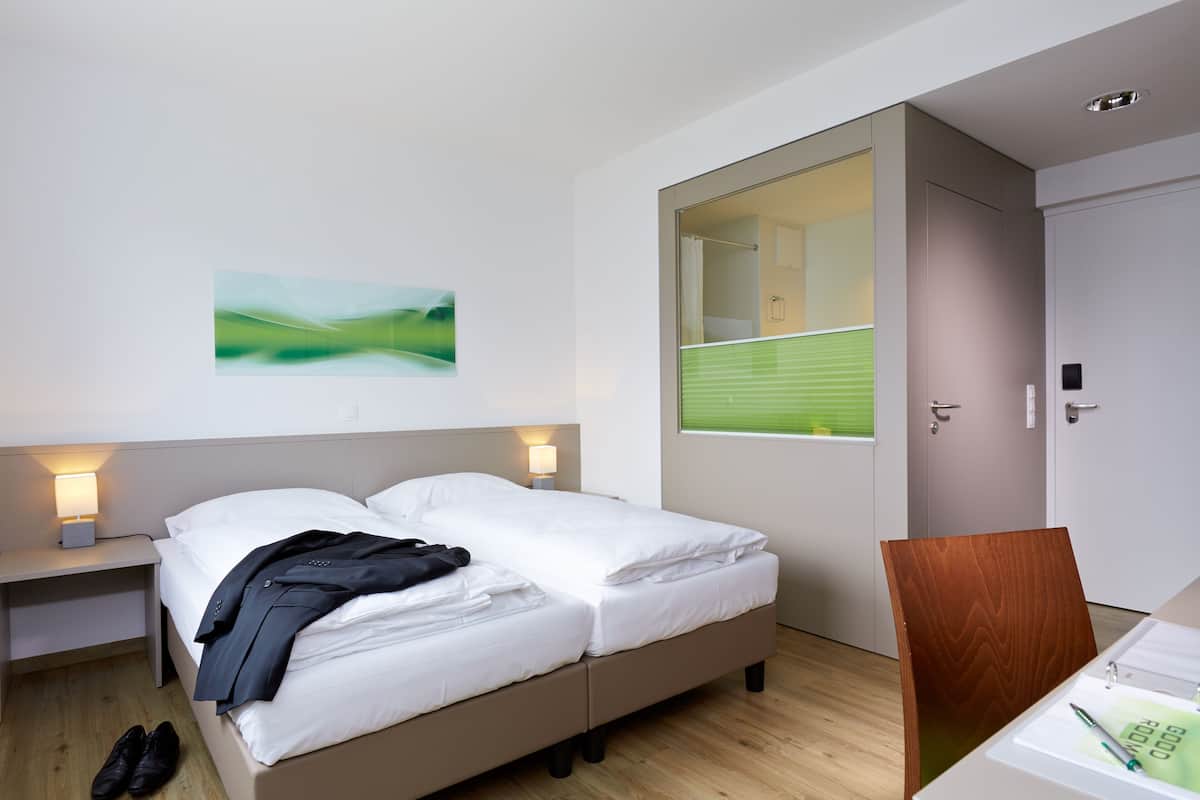 A modern hotel room with a bed, bedside tables, a desk, and a chair.
