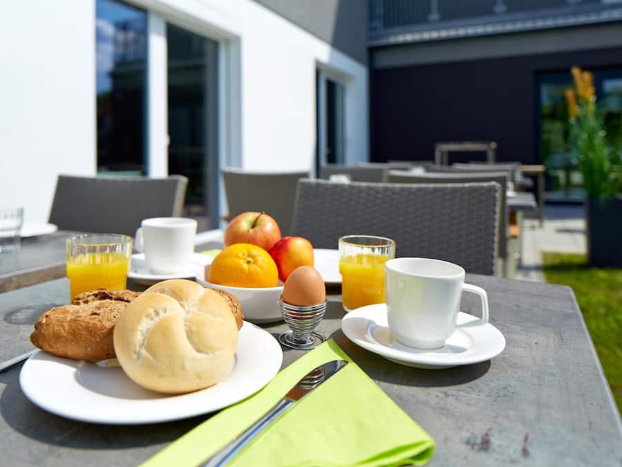 Un desayuno servido en una mesa al aire libre, con un plato de comida, una taza y un vaso de zumo de naranja.
