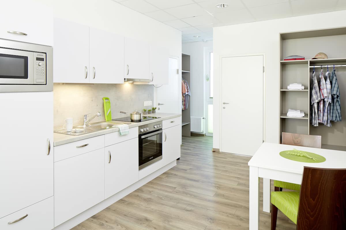 A modern kitchen with white cabinets, a microwave, and a dining area with a table and chairs.
