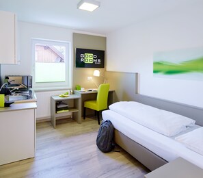 Una habitación de hotel con cama, escritorio, silla, televisor y radiador.