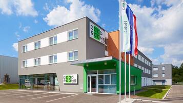 A modern building with a green entrance, labeled "GOOD ROOMS," and multiple flags including the French flag.