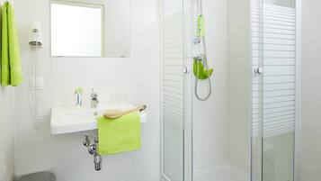 Un bagno moderno con doccia vetrata, lavandino bianco e asciugamano verde, oltre a uno specchio sopra il lavandino.