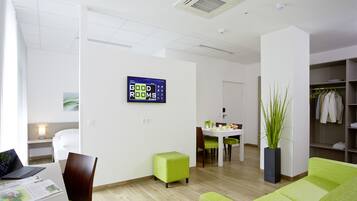 Habitación de hotel moderna con sofá verde, zona de comedor, pantalla de televisión y armario.