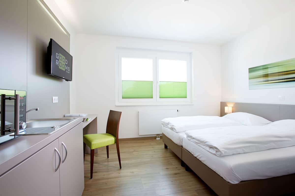 A hotel room with a kitchenette, a bed, a chair, and a window with blinds.