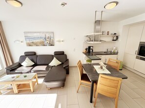 A modern living room with a sectional sofa, a dining table, and a kitchen area with a microwave and stove.