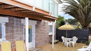 A patio area with a table and chairs, a covered seating area, and a view of a stone building. - Beachside 3-Star Apartment with WIFI and Parking, 20m from the Shore in Trégastel (Trégastel)
