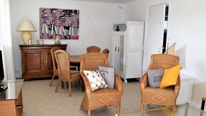 A living room with wicker furniture, a glass coffee table, and a dining table with chairs. - Beachside 3-Star Apartment with WIFI and Parking, 20m from the Shore in Trégastel (Trégastel)