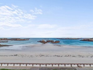 A beach with a clear sky, rocky formations in the water, and a sandy shore.