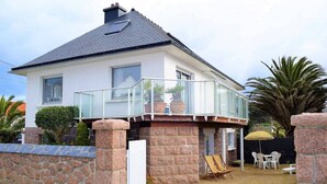 A two-story house with a balcony, stone walls, and a small patio area with outdoor furniture. - Beachside 3-Star Apartment with WIFI and Parking, 20m from the Shore in Trégastel (Trégastel)