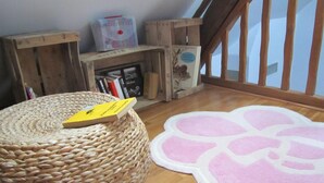 A cozy room with a wooden floor, a woven pouf, a pink and white rug, and a bookshelf with books and a framed picture. - Charming house near Tours, enclosed garden, perfect for families (Montlouis-sur-Loire)