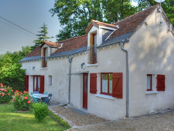 Une maison à deux étages, avec un toit en pente, des volets rouges et un petit balcon.