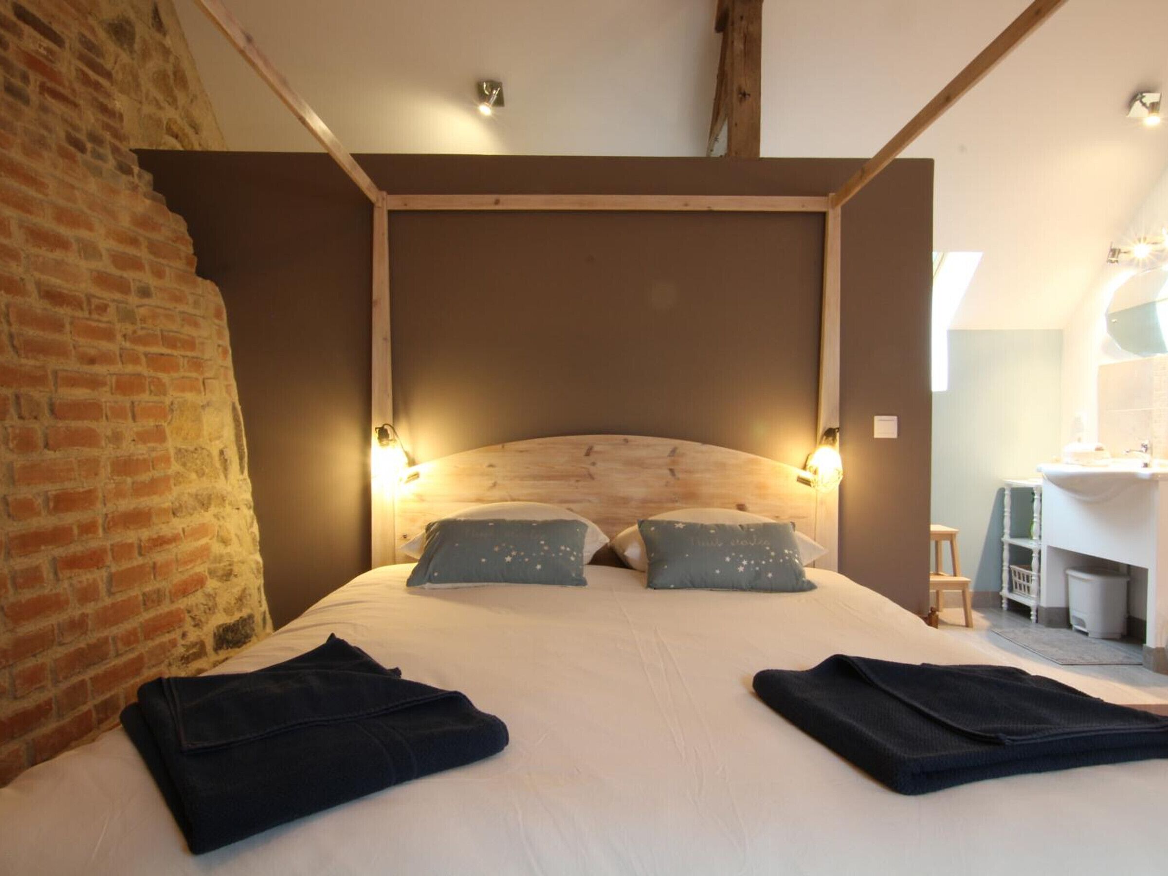 A bedroom with a wooden headboard, two pillows, a bed with a white sheet, and a neatly folded blanket on the bed.
