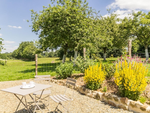 An outdoor seating area with a table and chairs, surrounded by a gravel path and a stone wall.