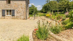 A stone building with a gravel driveway and a garden with various plants and flowers. - Charming Normandy cottage with wood stove and private yard (Bourguenolles)
