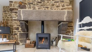 A cozy room with a stone fireplace, a television, and a fluffy chair. - Charming Normandy cottage with wood stove and private yard (Bourguenolles)