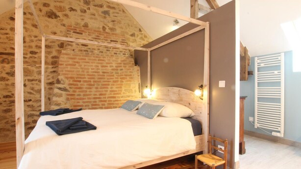 A bedroom with a four-poster bed, a wooden chair, and a brick wall. - Charming Normandy cottage with wood stove and private yard (Bourguenolles)