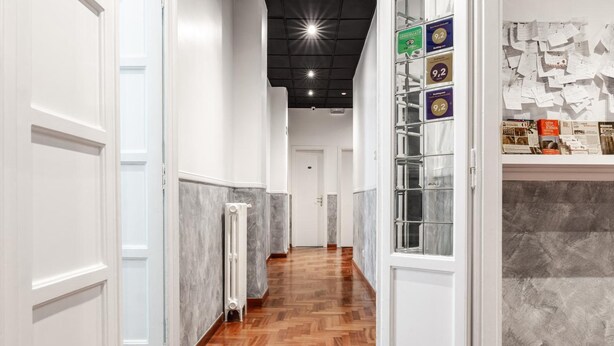 Un pasillo con piso de madera, paredes blancas y una zona de recepción con mostrador de mármol.