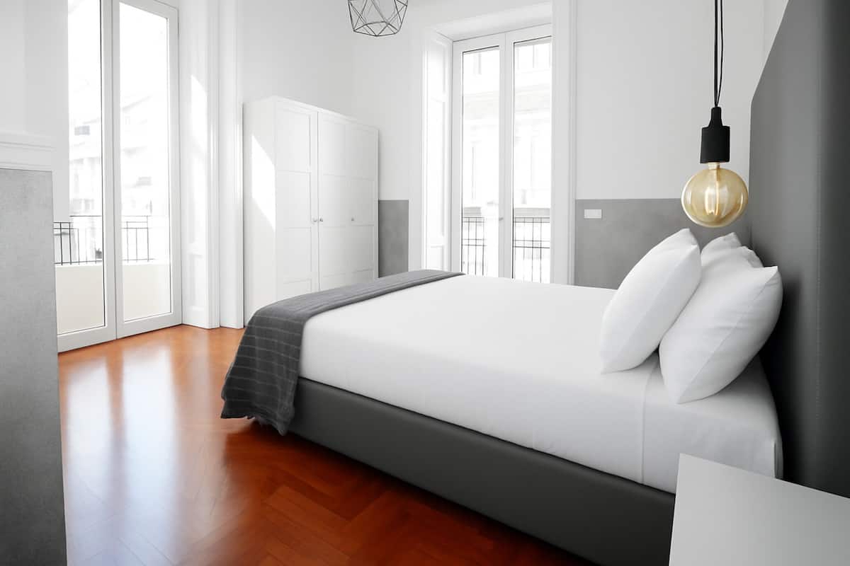 Un dormitorio moderno con una cama grande, ropa de cama blanca, un cabecero gris y una lámpara colgante.