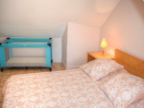 Une chambre avec un lit superposé et un lit simple, une table de chevet avec une lampe et un mur uni.