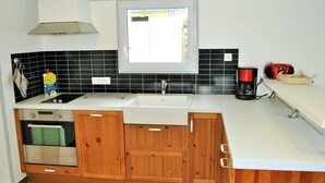 Eine moderne Küche mit Holzausstattung, einer weißen Arbeitsplatte, einem integrierten Backofen, einer Spüle und einem Fenster darüber.