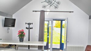 Eine moderne Küche mit weißer Arbeitsplatte, einem Blumentopf, einem Fernseher und einer Schiebeglastür, die in einen Garten führt.
