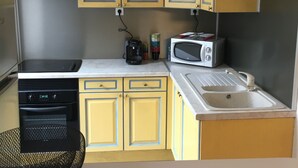 Una cocina compacta con gabinetes amarillos, una campana extractora negra, un microondas, un tostador y un lavamanos.