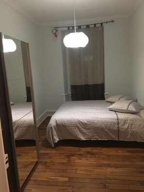 Un dormitorio con cama, espejo, lámpara colgante y ventana con cortina.