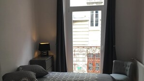 Un dormitorio con cama, mesita de noche, una silla y vistas al balcón exterior.