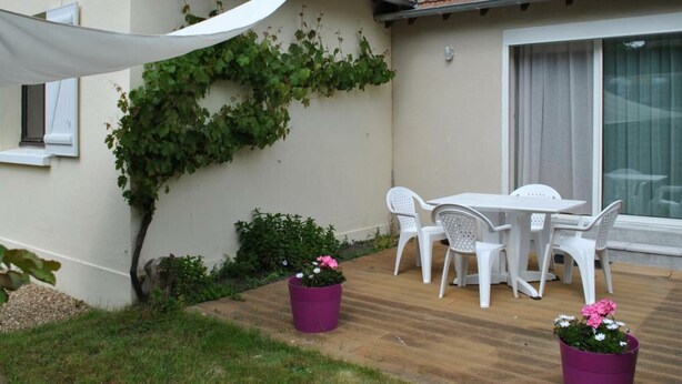 Eine Terrasse mit Tisch und Stühlen, einem weißen Sonnensegel und Blumentöpfen.