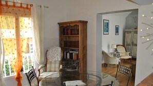 Ein Essbereich mit einem Glastisch, umgeben von Stühlen, einem Holzregal und einem Fenster mit Vorhängen.