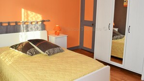 A bedroom with a bed, a nightstand, an orange wall, a wardrobe, and a door.