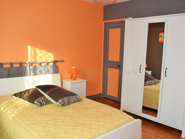 A bedroom with a bed, a nightstand, an orange wall, a wardrobe, and a door.