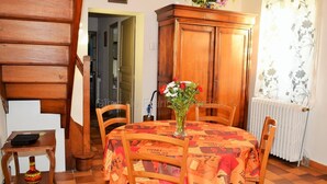 A dining area with a round table covered by a tablecloth, wooden chairs, a cabinet, and a vase with flowers.