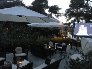 An outdoor seating area with tables and chairs, umbrellas, and a projection screen displaying an image. - Apartments Vojvoda (Kotor)