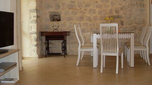A dining area with a stone wall, a wooden table, and white chairs. - Apartments Vojvoda (Kotor)