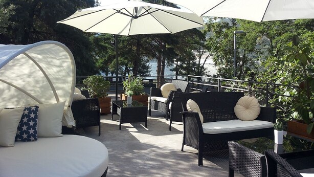 An outdoor seating area with wicker furniture, white cushions, and large umbrellas providing shade. - Apartments Vojvoda (Kotor)