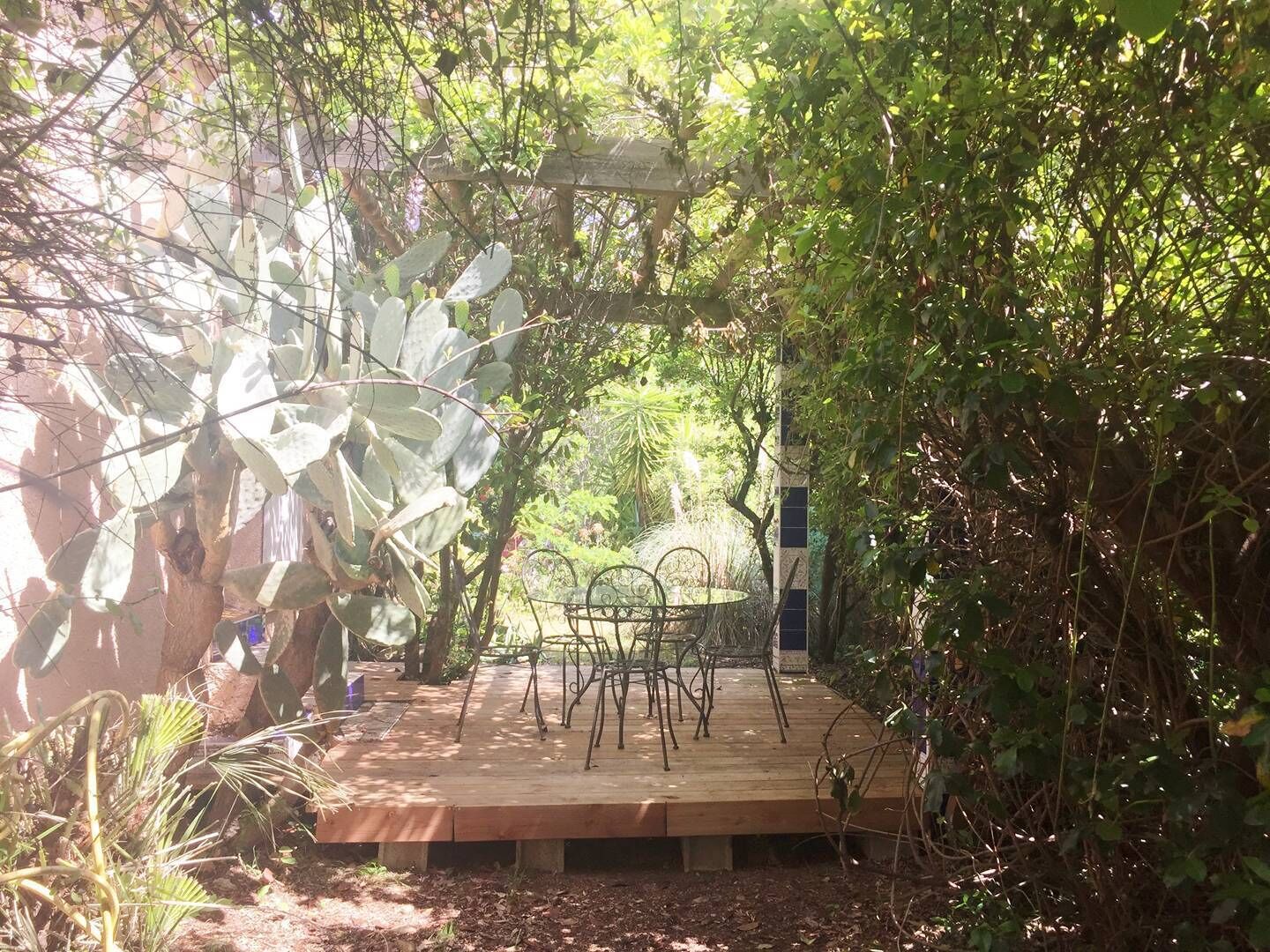 A wooden deck with metal chairs, surrounded by dense foliage and a pergola structure.