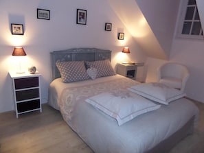 A bedroom with a bed, two bedside tables, a chair, and a sloped ceiling. - Spacious Cottage with Garden in Touraine Vineyards — Sleeps 10, Near Loire Castles (Cravant-les-Côteaux)