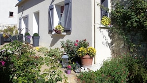 Ein weißes Gebäude mit grauen Fensterläden, Topfpflanzen und einer Steinmauer.