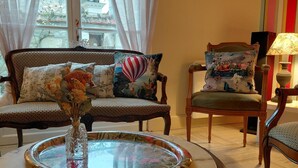 Ein Wohnzimmer mit Sofa, Sessel, Tisch mit Vase und Blick ins Freie durch ein Fenster.