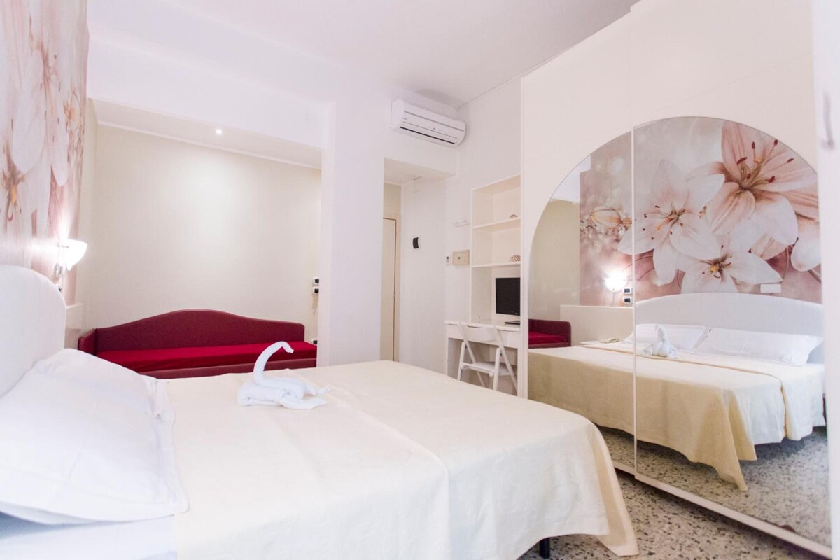 Une chambre d’hôtel avec un lit, un bureau, une chaise et un grand miroir.