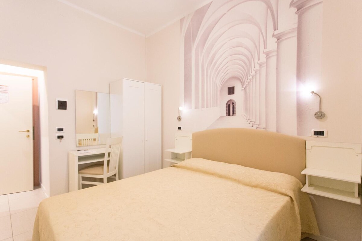 Une chambre d’hôtel comprenant un lit, un bureau, une armoire et un mur agrémenté d’une arche décorative.