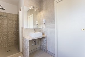 Une salle de bain équipée d’une douche, d’un lavabo et de deux sèche-cheveux fixés au mur.