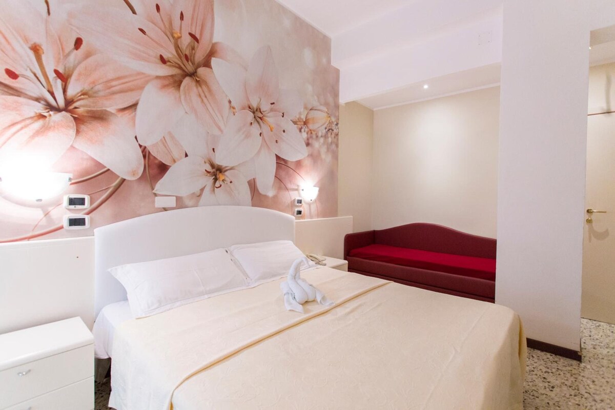 Een hotelkamer met een bed, een rode bank, een wand met bloemenbehang en bedlampen.