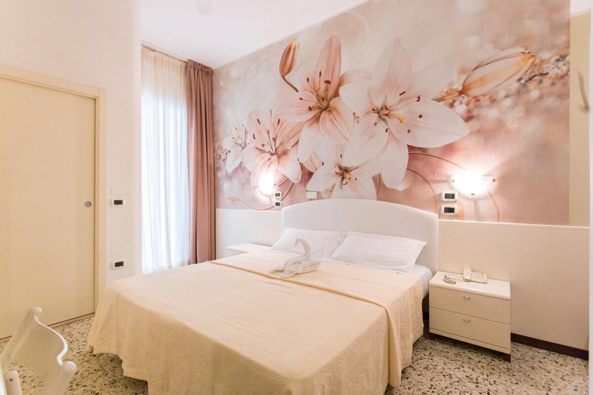 Een hotelkamer met een bed, een nachtkastje, een telefoon en een muur met een bloemenmural.