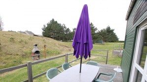 An outdoor patio with a table and chairs, a purple umbrella, and a view of a grassy hill and trees. - Cozy Family Retreat: 2BR, Terrace, BBQ, Near Granville, Pet-Friendly (Bréhal-Saint-Martin de Bréhal)